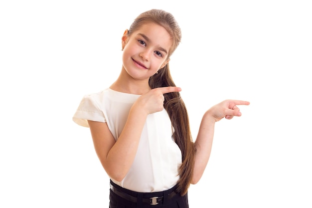 Little nice girl with long brown ponytail in Tshirt and black skirt showing two fingers  in studio