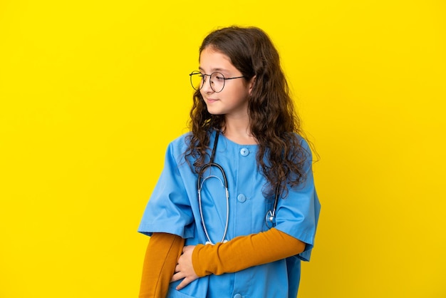 Little nurse girl isolated on yellow background looking side