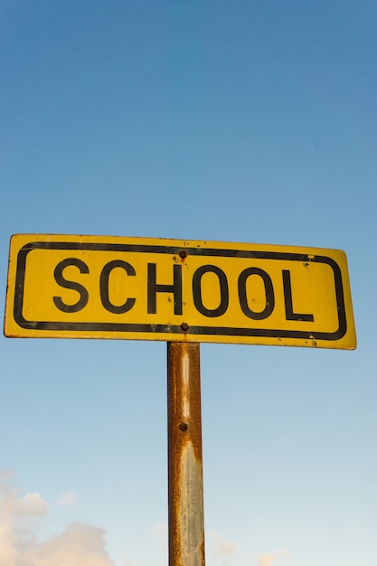 A little old yellow school sign with a beautiful blue sky in the background and some clouds