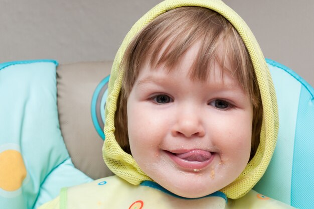 A little one year old baby girl is eating the highchair.