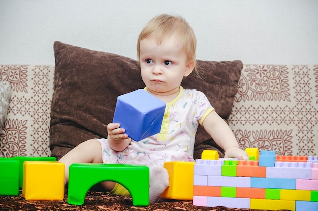 A little oneyearold girl is sitting on the sofa and playing with cubes