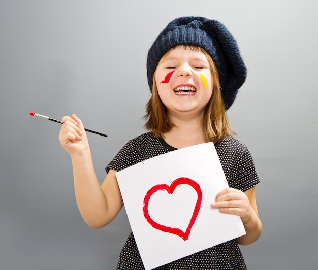 Piccola ragazza pittore con un cuore disegnato isolato su grigio