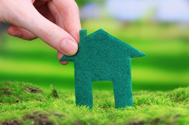 Little paper house in hand on green grass on bright background