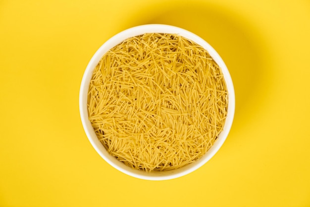 Little pasta for soup in a plate on yellow background