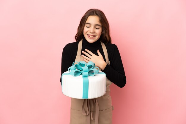 Little Pastry chef holding a big cake isolated on pink background smiling a lot