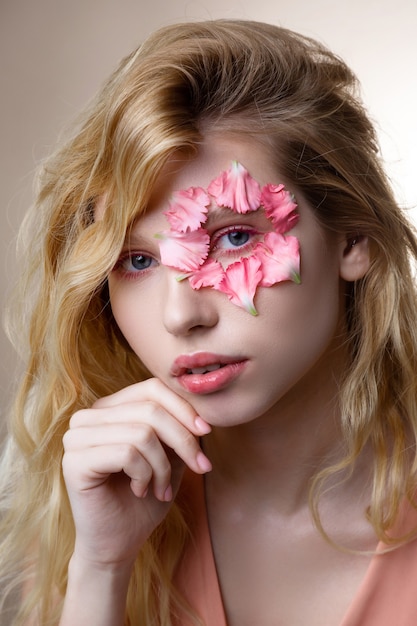 Little petals. Tender blue-eyed woman with blonde wavy hair having little pink petals around her eye