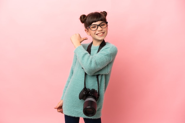 Маленькая девочка-фотограф изолирована на розовой стене, гордая и самодовольная
