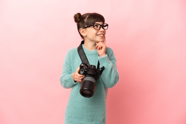 Foto piccola ragazza del fotografo isolata sulla parete rosa che pensa un'idea mentre osserva in su