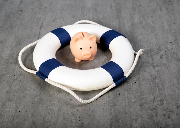 Little piggy bank inside of lifebuoy Safe Money Blue and white life buoy on wooden desk table background Assets wealth money saving and security by insurance concept Copy space Safe box