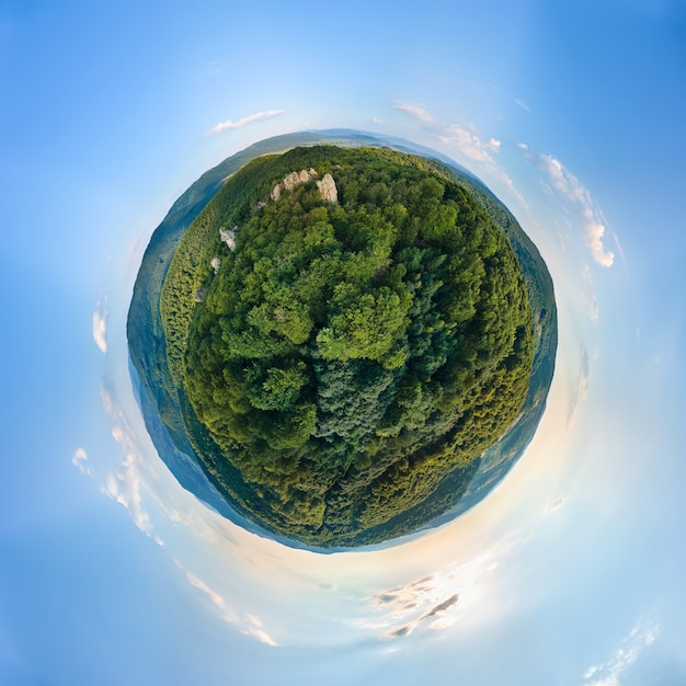 Little planet globe with dark mountain hills covered with green mixed pine and lush woods surrounded with clear blue sky with white clouds.