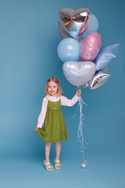 Little positive girl with balloons on a blue surface