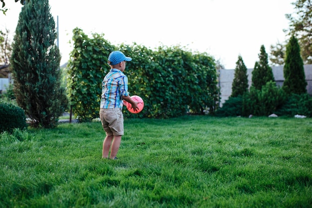 Little preschool boy playing soccer on the backyard lawn