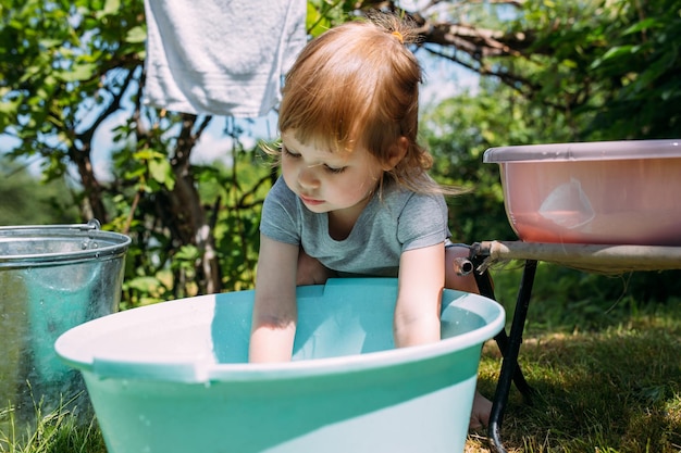 Little preschool girl helps with laundry child washes clothes in garden