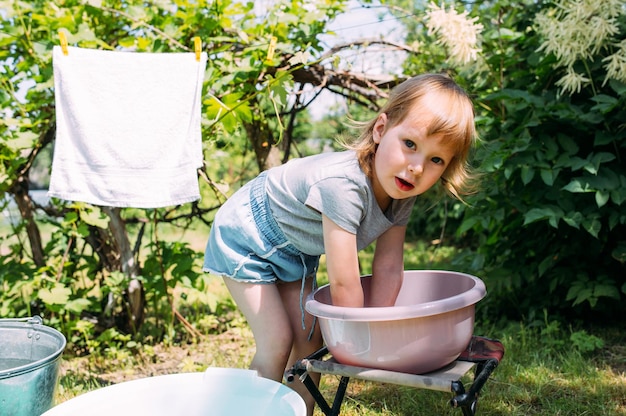 어린 미취학 아동은 정원에서 세탁하는 아이가 옷을 씻는 것을 돕습니다.