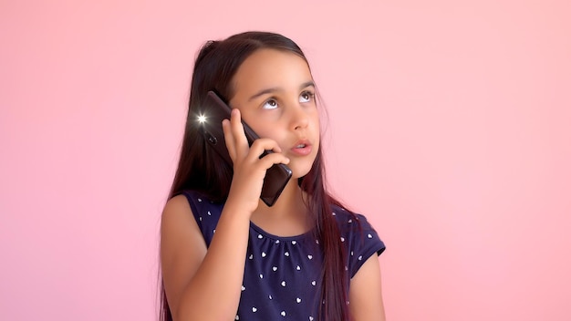 Bambina in età prescolare in un vestito che tiene un telefono cellulare, isolata sopra il rosa