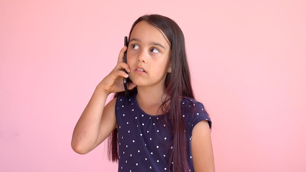 Little preschooler girl in a dress holding a mobile phone, isolated over pink