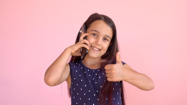 Little preschooler girl in a dress holding a mobile phone, isolated over pink