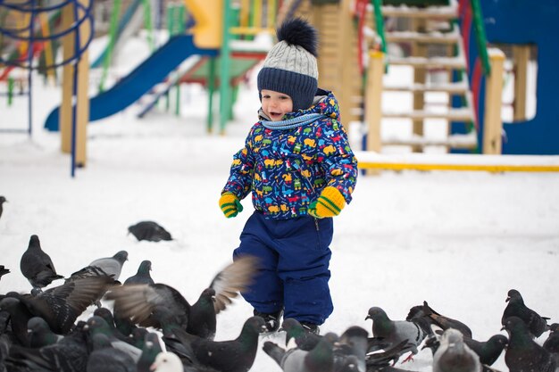 Little pretty boy feeds birds in winter snow park outdoor