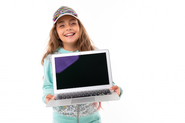 Little pretty caucasian girl in a tracksuit holds new laptop, picture isolated on white wall