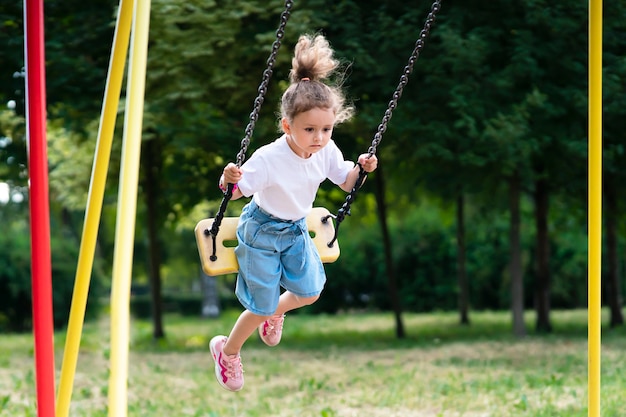 Little pretty girl, cute kid, child is swinging on a swing at summer sunny weather in a park, playing in the children playground