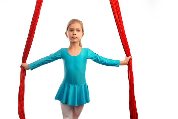 Bambina graziosa che si prepara per le prestazioni su nastri rossi ariosi su sfondo bianco. concetto di acrobazie e buon stretching per i bambini. luogo della pubblicità