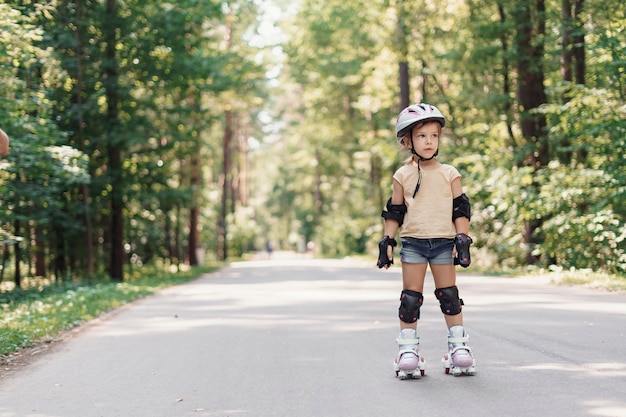 Little pretty girl on roller skates in helmet at a park.