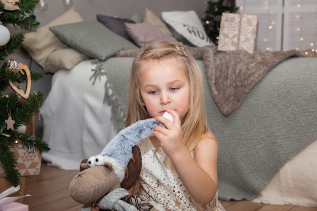 Una bambina carina con regali di natale seduta vicino all'albero di natale nella stanza, concetto di capodanno