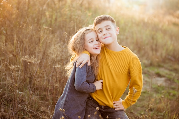 Little pretty girl and young boy hugging each other on autumn day. Brother and little sister cuddling. Happy family