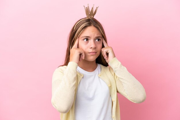 Little princess with crown isolated on pink background having doubts and thinking