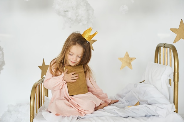 Little princess with a magic wand on а bed in a cloud on a white background