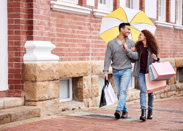 少しの雨でも買い物は止まらない愛情のこもった若いカップルが街で買い物を楽しんでいる様子のフルレングスショット