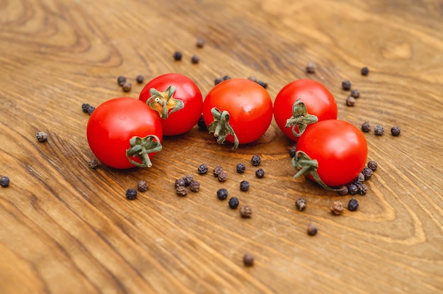 Little red cherry tomatoes on wooden board background Scattered pepper peas