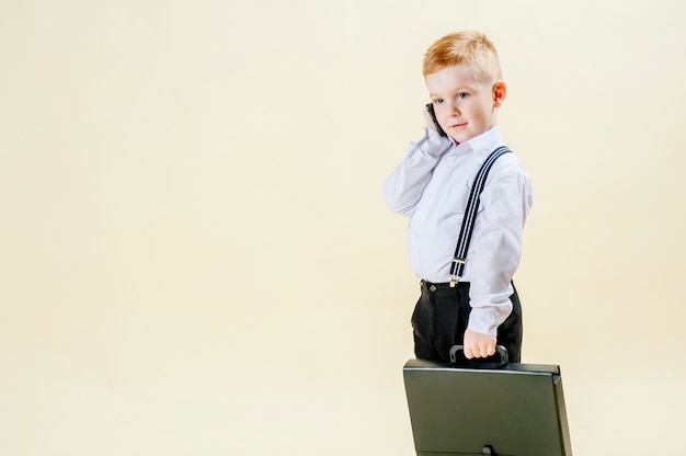 Маленький рыжий мальчик в деловом костюме с телефоном в руке спешит на встречу в деловом костюме, бизнес, мини-босс