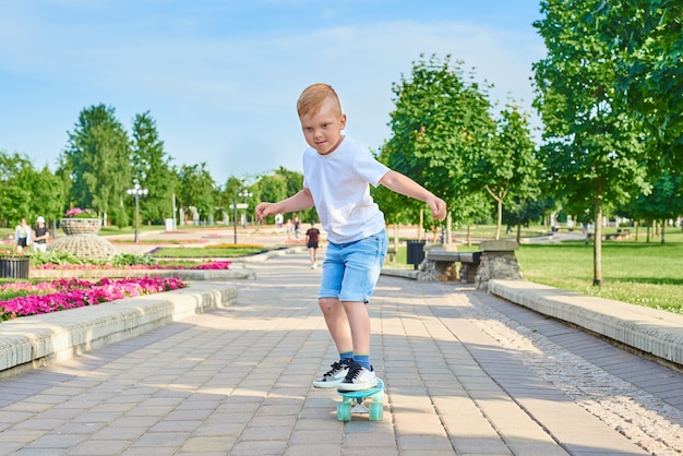 Little red-haired boy learns to skate in the park in the summer