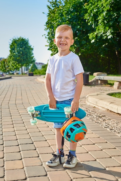 Little red-haired boy learns to skate in the park in the summer