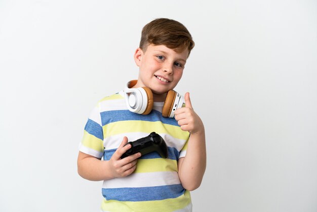 Little redhead boy holding a game pad isolated on white background giving a thumbs up gesture