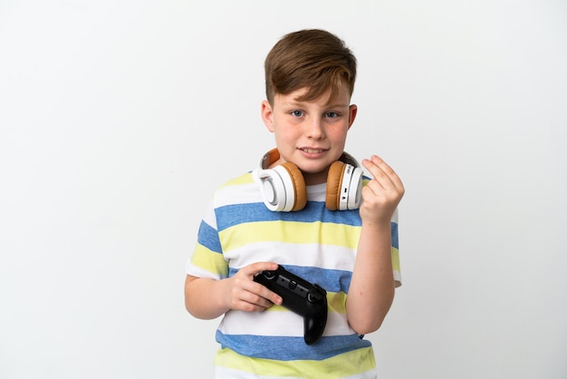 Little redhead boy holding a game pad isolated on white background making money gesture