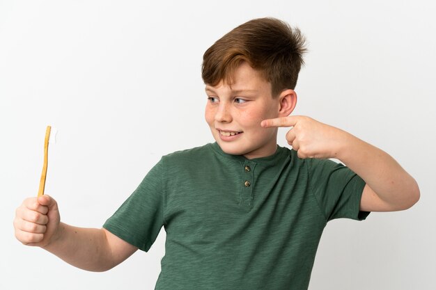 Little redhead boy holding a toothbrush isolated on white background and pointing it