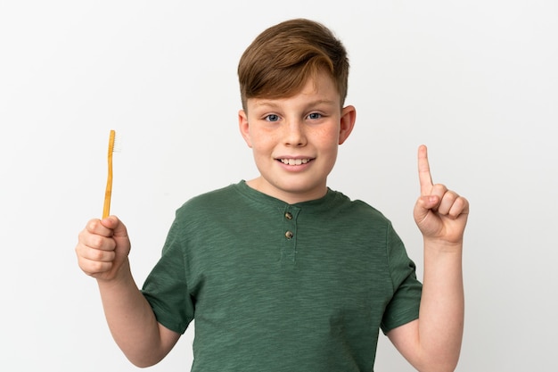 Little redhead boy holding a toothbrush isolated on white background pointing up a great idea