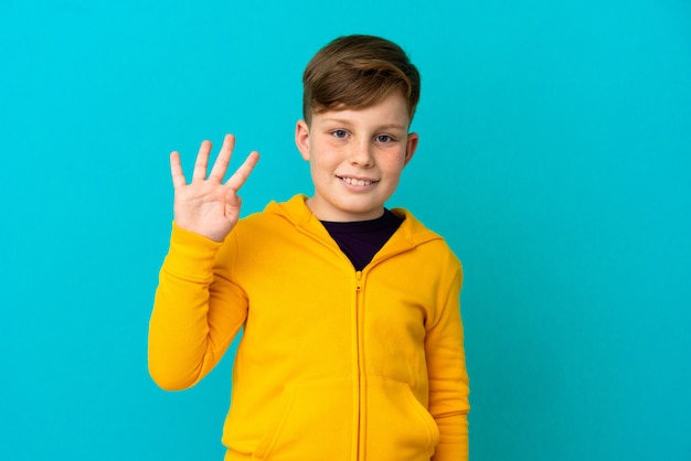 Little redhead boy isolated on blue background happy and counting four with fingers