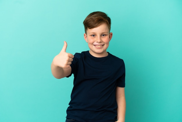 Little redhead boy isolated on blue background with thumbs up because something good has happened