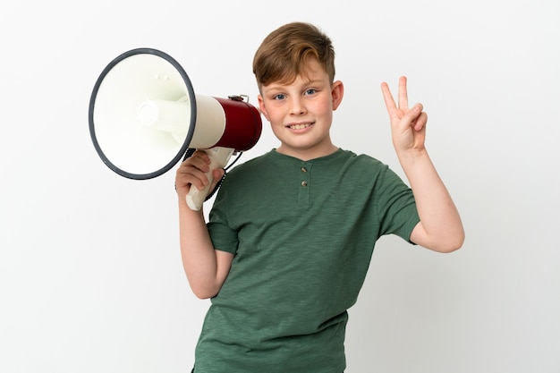 Маленький рыжий мальчик, изолированные на белом фоне, держит мегафон и улыбается и показывает знак победы