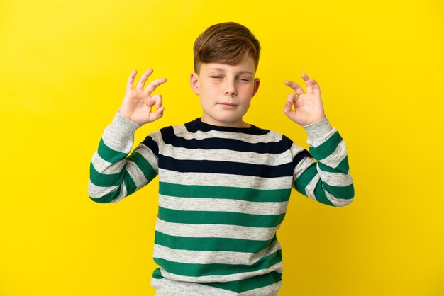 Little redhead boy isolated on yellow background in zen pose