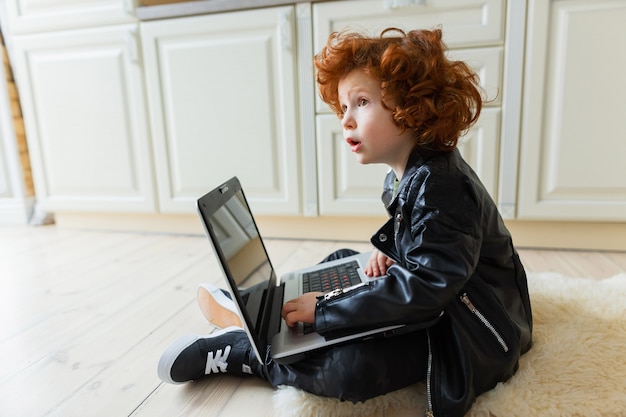 Little redhead boy uses a laptop