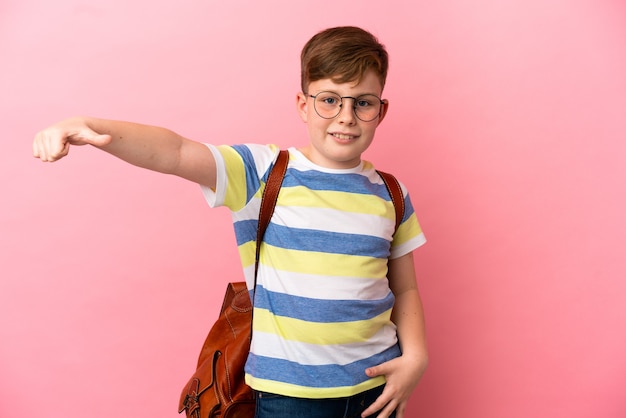 Little redhead caucasian boy isolated on pink background giving a thumbs up gesture