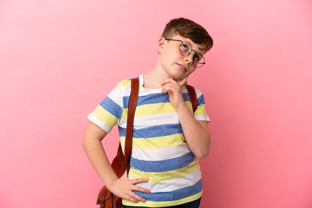 Little redhead caucasian boy isolated on pink background thinking an idea while looking up