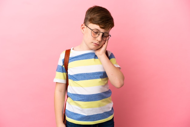 Little redhead caucasian boy isolated on pink background with headache