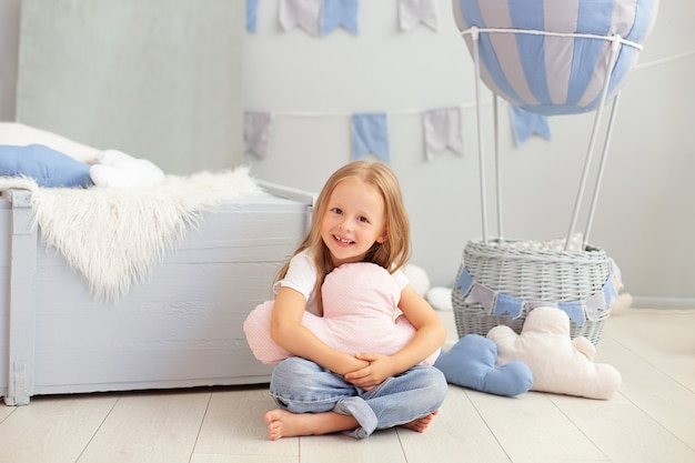 Little redhead girl sit on floor hugging cloud pillow against decorative balloon.