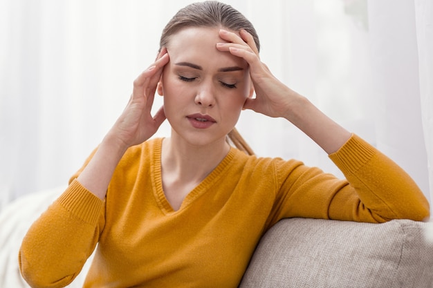 Little relief. Brunette adorable stressful woman caressing her head while relaxing and closing her eyes