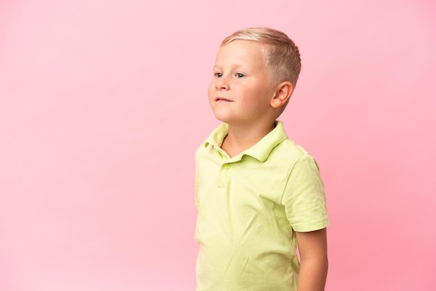 Фото Маленький русский мальчик, изолированный на розовом фоне, смотрит вверх, улыбаясь